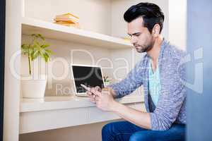 Thoughtful man using smartphone and laptop