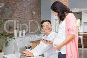 Smiling pregnant woman showing tablet to her husband