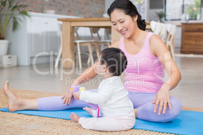 Happy mother exercising on mat while looking at baby daughter