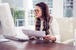 Focused Asian woman holding document and looking at computer mon