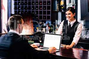 Businessman talking to barmaid and using laptop