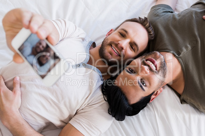 Happy gay couple taking selfie on bed