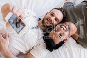 Happy gay couple taking selfie on bed