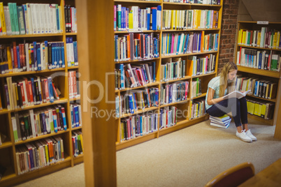 Blonde student reading while sitting on books