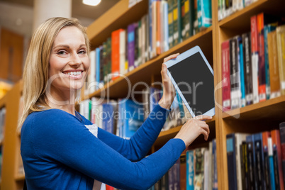 Female student tidying a tablet in a bookshelf