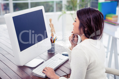 Asian woman on computer with finger on chin