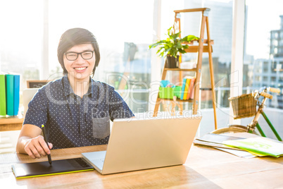 Smiling hipster businessman using laptop and graphic tablet