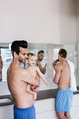 Happy gay couple shaving and holding their child