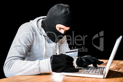 Focused thief with hood typing on laptop