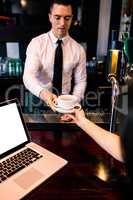 Barman giving coffee to customer with laptop