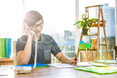 Smiling hipster businessman writing and holding telephone