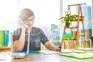 Smiling hipster businessman writing and holding telephone