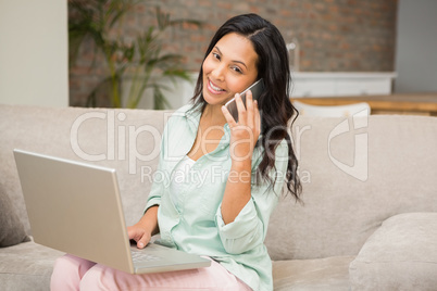 Smiling brunette on a phone call using laptop