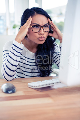 Frowning Asian woman looking at computer monitor with hands on h