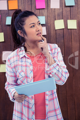 Thoughtful woman with finger on chin holding tablet