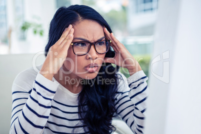 Frowning Asian woman looking at laptop with hands on head