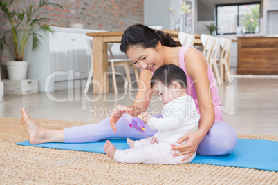 Happy mother and baby daughter sitting on exercising mat