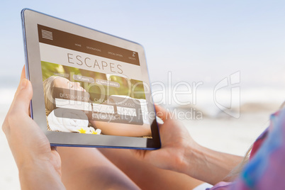 Composite image of woman sitting on beach in deck chair using ta