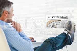 Composite image of relaxed man with feet on desk using computer