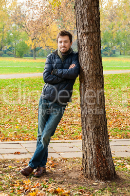 Handsome guy leaned against a tree in autumn park