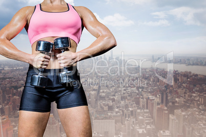 Composite image of portrait of healthy woman exercising with dum
