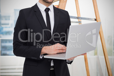 Composite image of mid section of a businessman using laptop