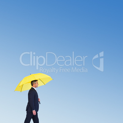 Composite image of businessman with yellow umbrella walking on w