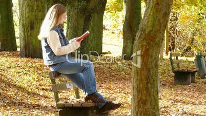 woman is reading a book on a bench in autumn