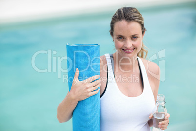 Pregnant woman holding water bottle and mat