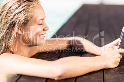 Blonde leaning on pools edge and using smartphone