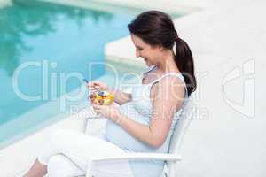 Smiling pregnant woman eating fruit