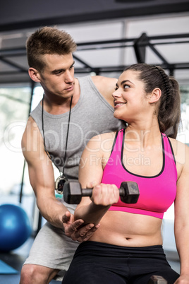 Male trainer assisting woman lifting dumbbells