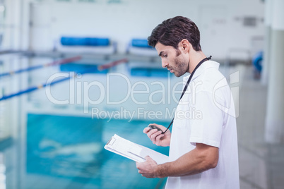Handsome trainer holding stopwatch and reading clipboard Handsome trainer holding stopwatch and reading clipboard