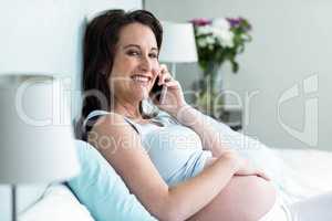 Pregnant woman lying in bed making a phone call