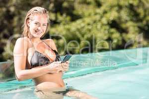 Smiling blonde using smartphone in the pool