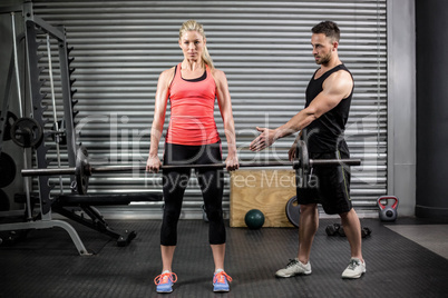 Trainer helping woman with lifting barbell