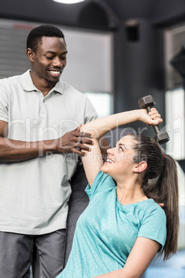 Athletic woman lifting weights helped by trainer