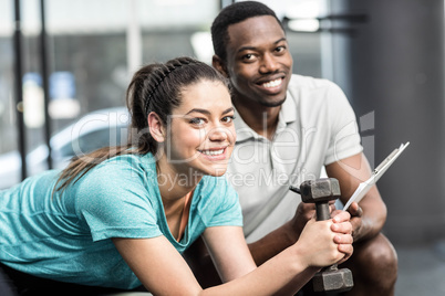 Athletic woman lifting weights helped by trainer