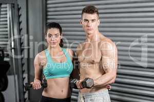 Fit couple lifting dumbbells and looking at the camera