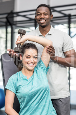 Athletic woman lifting weights helped by trainer