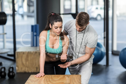 Male trainer assisting woman lifting dumbbells