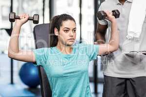 Athletic woman lifting weights helped by trainer