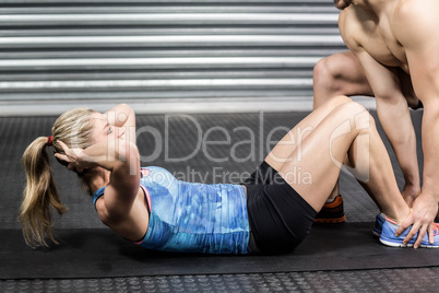 Male trainer assisting woman with sit ups