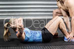 Male trainer assisting woman with sit ups