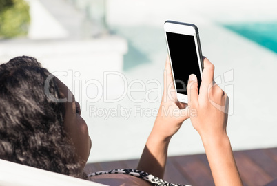 Fit brunette lying on deck chair and using smartphone