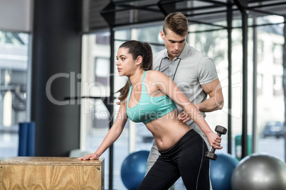 Male trainer assisting woman lifting dumbbells