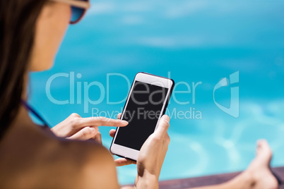 Brunette using smartphone poolside