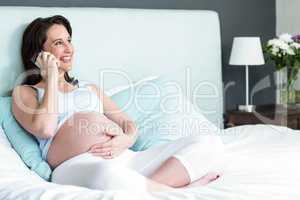 Pregnant woman lying in bed making a phone call