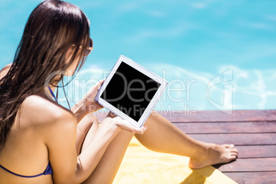 Brunette using tablet poolside