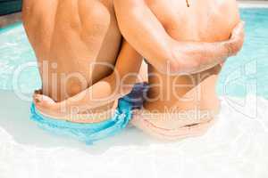 Mid section of couple embracing while sitting on pool edge